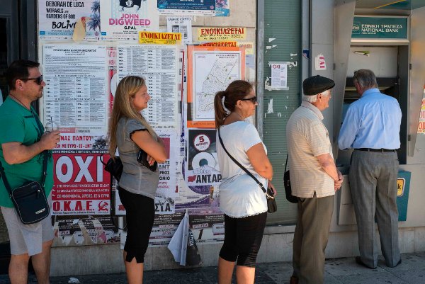 Am Tag des Referendums bilden sich lange Schlangen vor den Geldautomaten. Genug Zeit, die Plakate im Hintergrund zu betrachten, die für ein „Nein“ bein bei der Abstimmung werben.